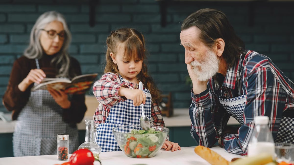 Grandfather and granddaughter making salad while grandmother reads a recipe.